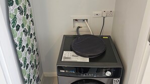 Un espace buanderie comprenant un lave-linge et un sèche-linge, une étagère avec des produits de nettoyage et un étendoir.