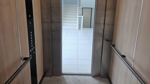 L’intérieur d’un ascenseur, avec un panneau de commande et une vue sur un sol carrelé menant à un escalier.
