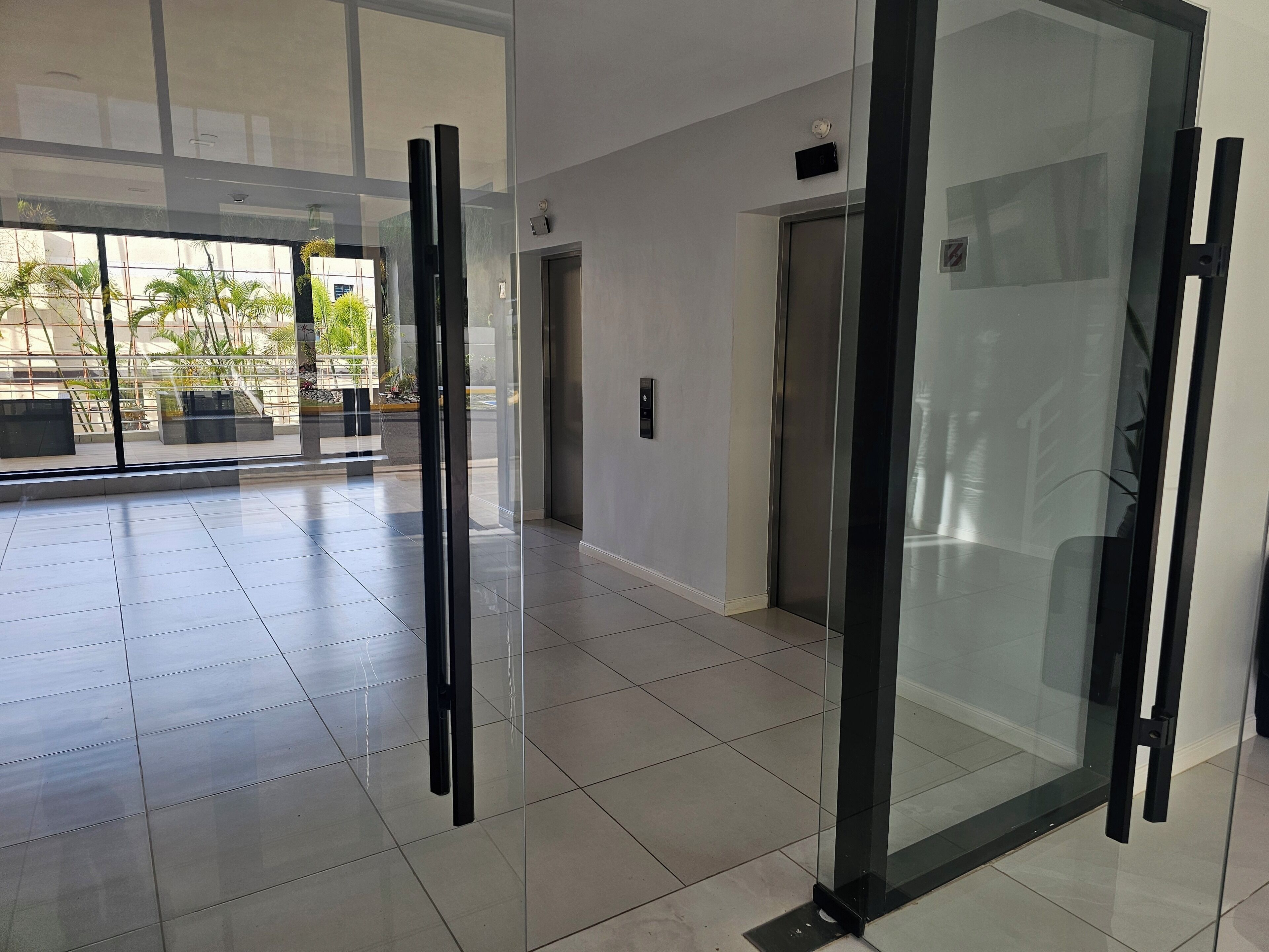 Et moderne interiør med glas elevator, en dør og udsigt til udendørs beplantning.