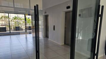 Et moderne interiør med glas elevator, en dør og udsigt til udendørs beplantning.