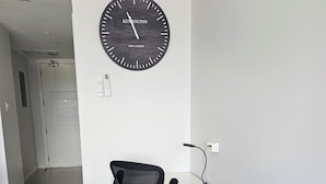 Un espace de bureau moderne avec une horloge noire au mur, un bureau blanc, un fauteuil de bureau noir et un canapé blanc.