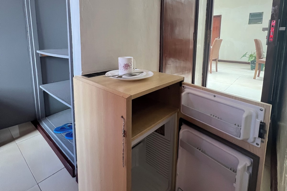 A compact kitchenette with a microwave, a small refrigerator, and a wooden counter with a cup and spoon.