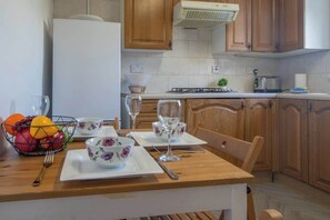 Une cuisine avec des meubles de rangement en bois, un réfrigérateur blanc, une cuisinière à gaz et une table à manger dressée avec des assiettes, des bols et des verres à vin.