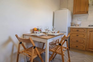 A small kitchen with a white refrigerator, wooden cabinets, a dining table with four chairs, and a fruit bowl on the counter. - Ashgrove House - 3 bedroom in Coatbridge (Coatbridge)