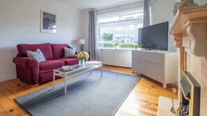 Een woonkamer met een rode bank, een salontafel, een televisie en een open haard.
