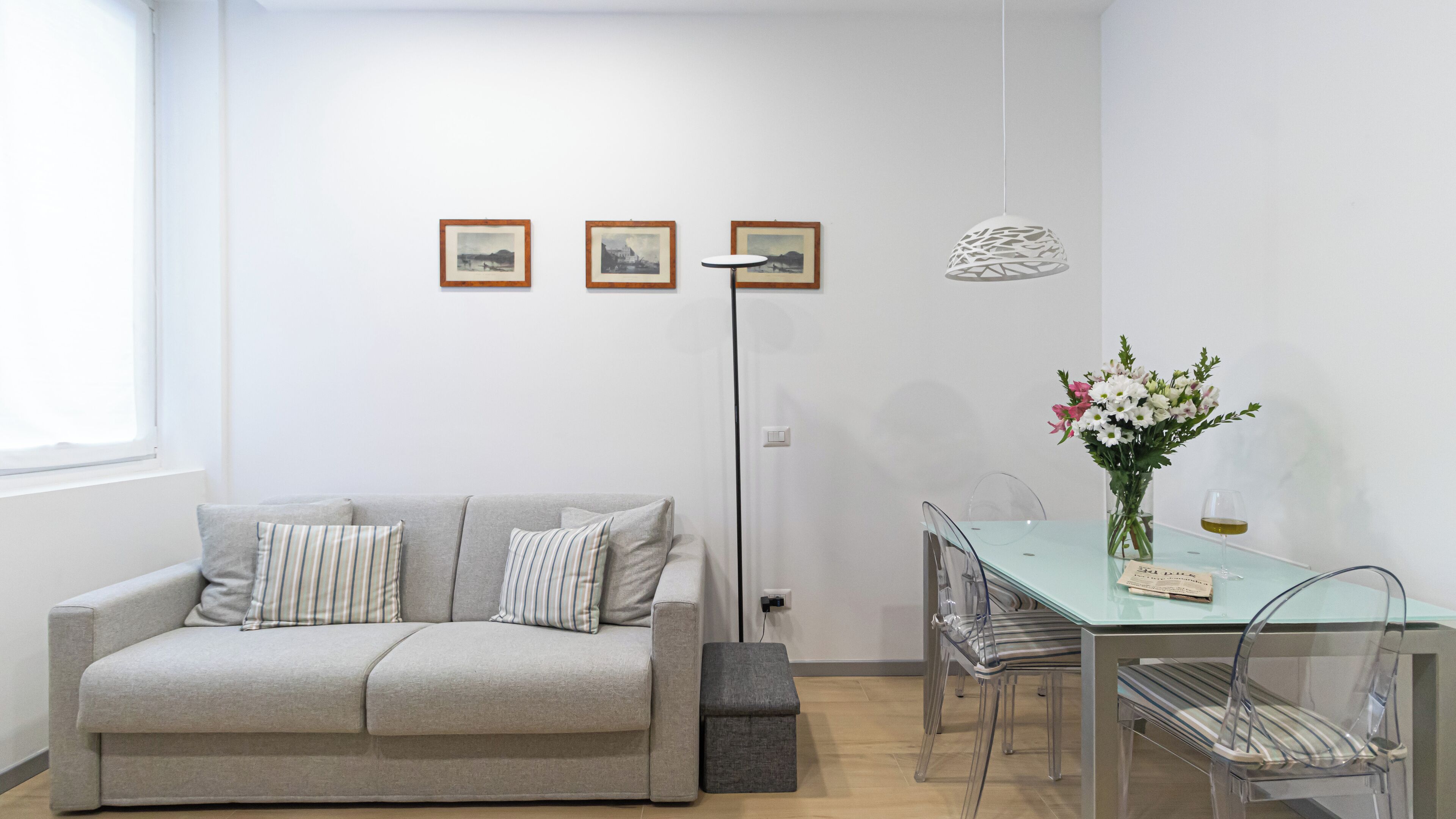 A modern living room with a grey sofa, a glass dining table, and a vase of flowers.