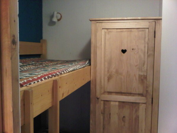A wooden bunk bed with a patterned bedspread and a wardrobe with a heart-shaped cutout.