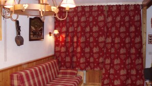 A cozy living room with a striped sofa, a wooden bench, a wall-mounted lamp, and a red curtain with a heart and tree pattern. - Les Ménuires, on skis (Saint Martin de Belleville)