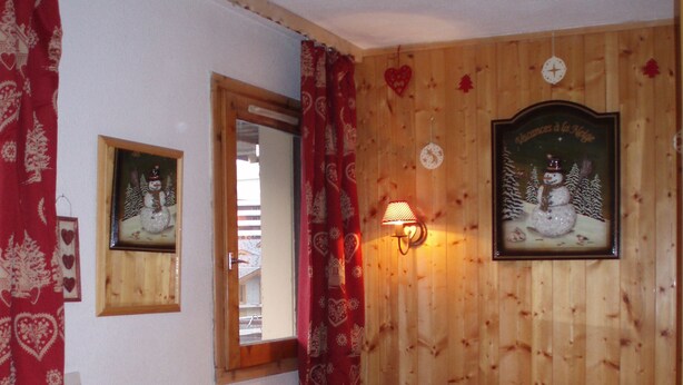 A cozy room with a wooden wall, a plaid sofa, a television on a wooden stand, and a framed picture of a snowman. - Les Ménuires, on skis (Saint Martin de Belleville)