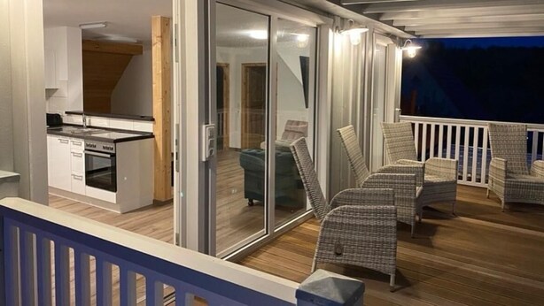 Ein Balkon mit Korbmöbeln und einer Schiebetür zu einer Küche.
