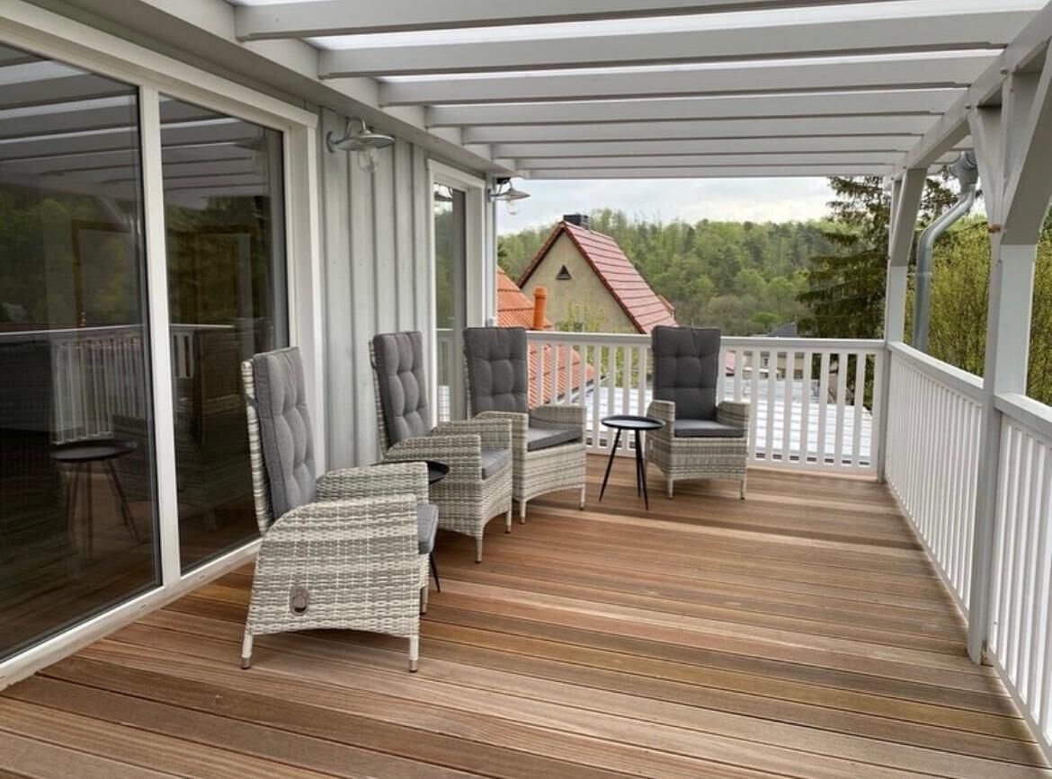 A covered outdoor deck with wicker furniture and a view of a house in the background.
