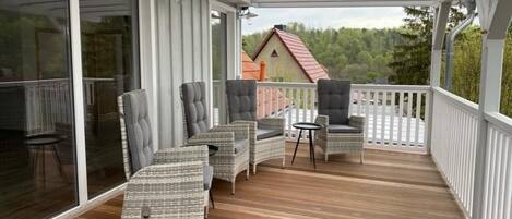 A covered outdoor deck with wicker furniture and a view of a house in the background.
