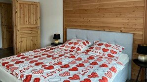 Ein Schlafzimmer mit einem Holzkopfteil, einem Bett mit Bettdecke mit Herzmuster und einem Nachttisch mit Lampe.