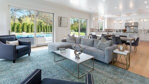 A spacious living room with a grey sofa, a coffee table, and a view of a swimming pool. - 6,400 square foot traditional-style home with a private pool and sweeping... (Southampton)