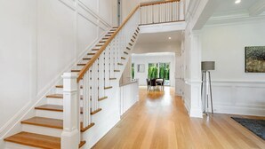A spacious hallway with a wooden staircase leading to an upper floor. - 6,400 square foot traditional-style home with a private pool and sweeping... (Southampton)
