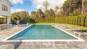 A rectangular swimming pool with clear water, surrounded by a stone deck. There are lounge chairs and a seating area with cushions. - 6,400 square foot traditional-style home with a private pool and sweeping... (Southampton)