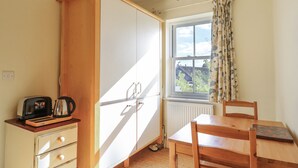 A compact kitchen with a built-in oven, a small dining table, and a window with curtains. - Over Village Studio (Cambridge)