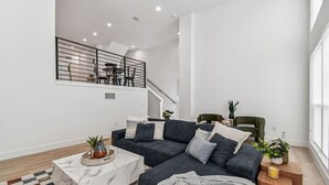 Ein modernes Wohnzimmer mit einem Ecksofa, einem Marmor-Couchtisch und einer Treppe, die in einen oberen Bereich führt.