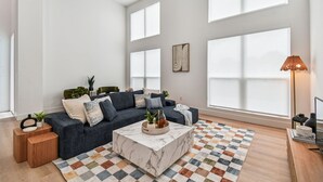 Ein geräumiges Wohnzimmer mit einem dunkelblauen Modulsofa, einem Marmor-Couchtisch und einem Schachbrettmuster-Teppich.