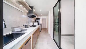 A modern kitchen with a long countertop, a built-in oven, and a glass door leading to a balcony. - Villa 35 Wongamat 4 BR, 300m from BEACH (Pattaya City)