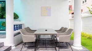 Een terras buiten met een tafel en vier stoelen, een bord op de muur, en een zwembad op de achtergrond.