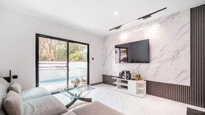 Ein modernes Wohnzimmer mit einer Couch, einem Glastisch und einem an einer Marmorwand montierten Fernseher.