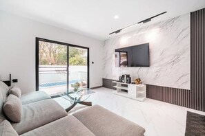 Un salon moderne avec un canapé, une table basse en verre et un téléviseur fixé sur un mur en marbre.