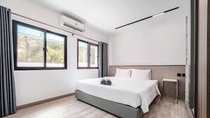 A modern hotel room with a large bed, a bedside table, and two windows with curtains. - Villa 35 Wongamat 4 BR, 300m from BEACH (Pattaya City)