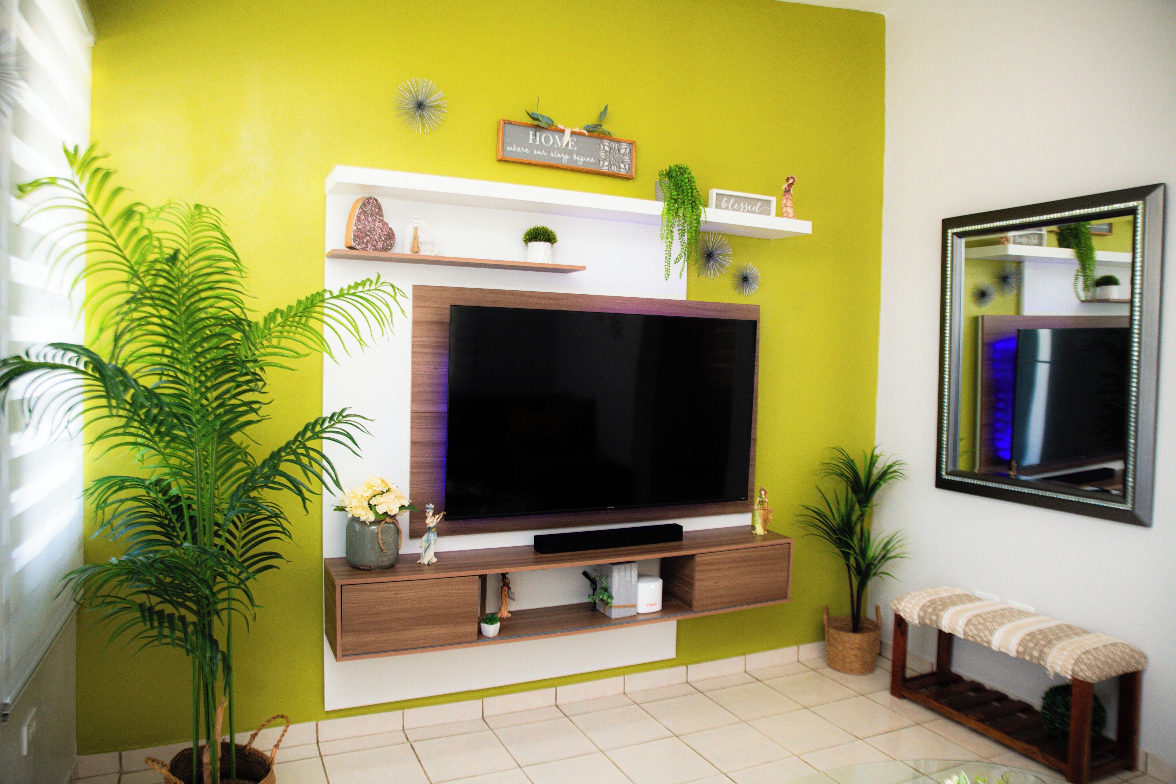 Un soggiorno con un'ampia televisione a schermo piatto, un mobile TV in legno, piante in vaso e una panca.