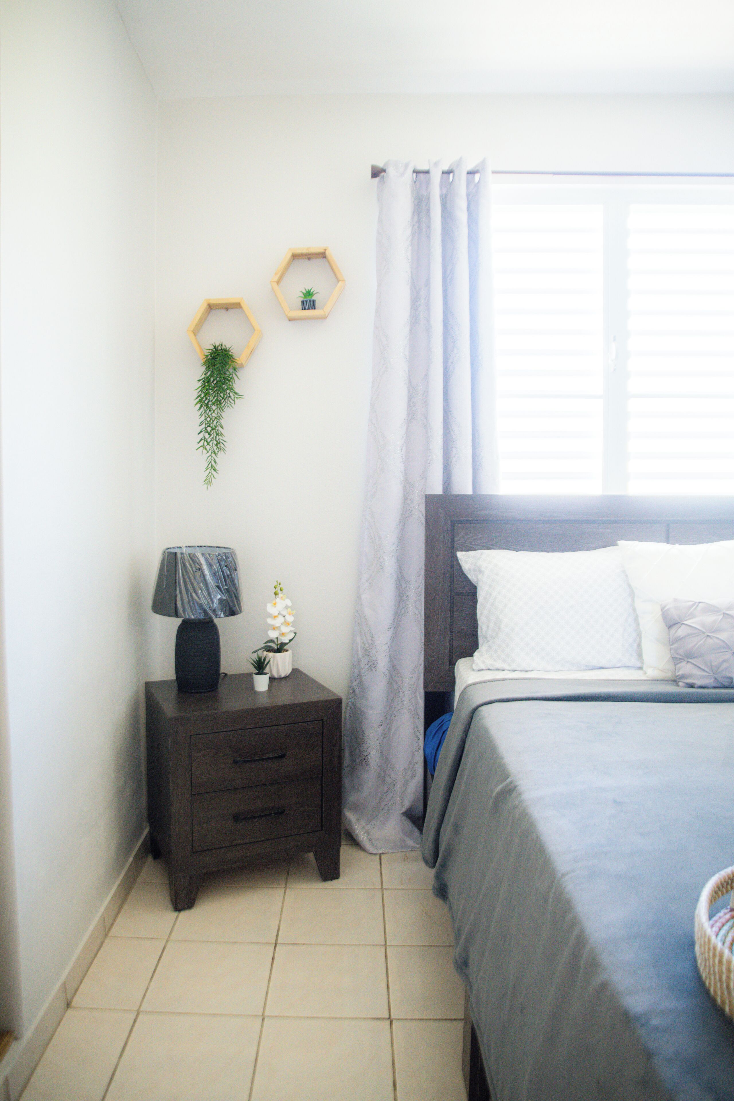 A bedroom with a bed, a nightstand with a lamp, and two hexagonal wall decorations.