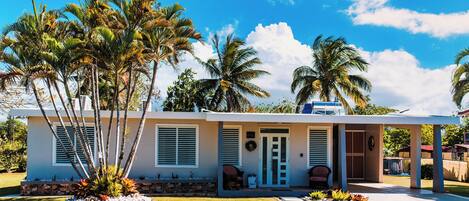 Una casa moderna con un porche cubierto, palmeras y un cielo azul despejado.