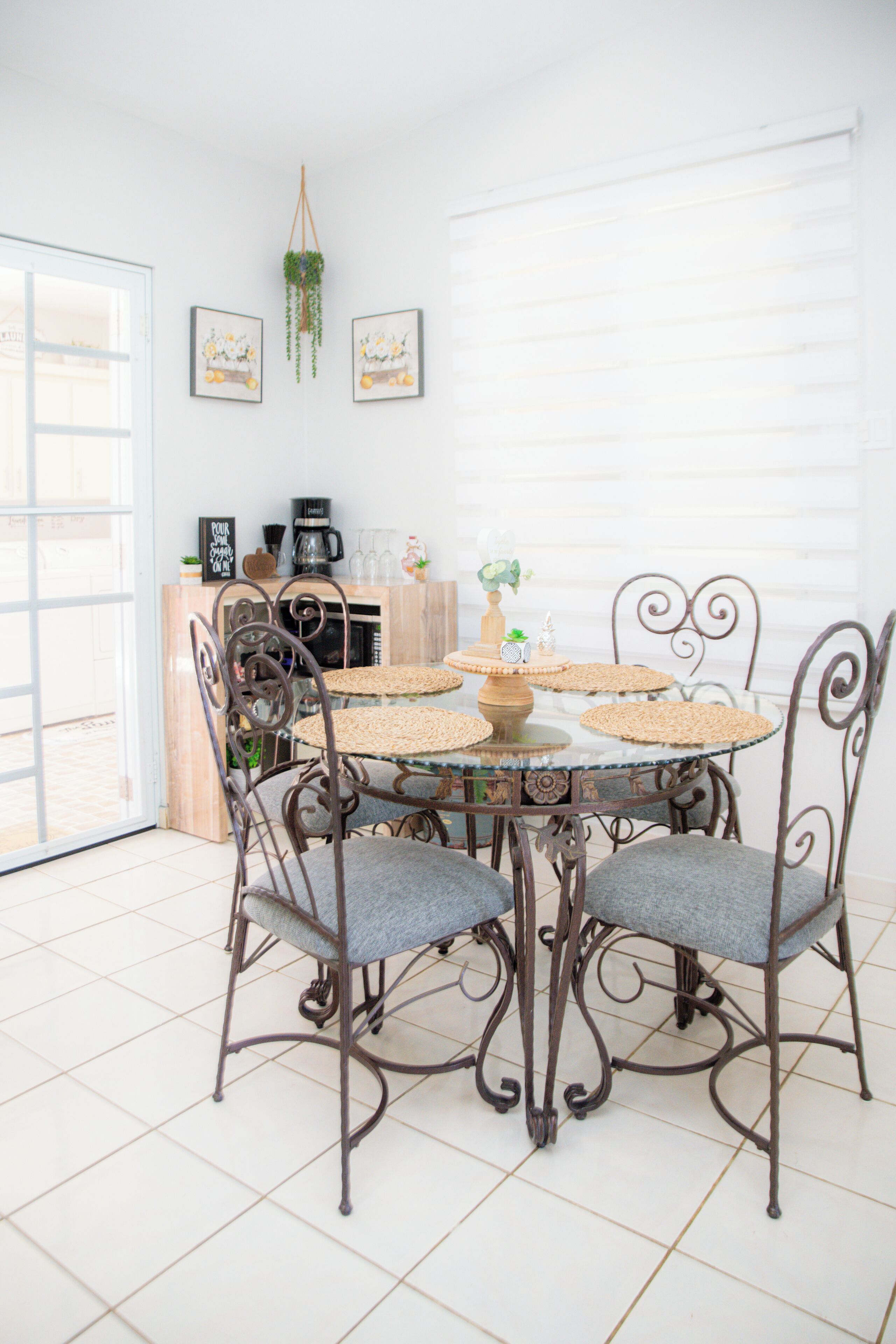 A dining area with a round table, four chairs, and a coffee station in the background.