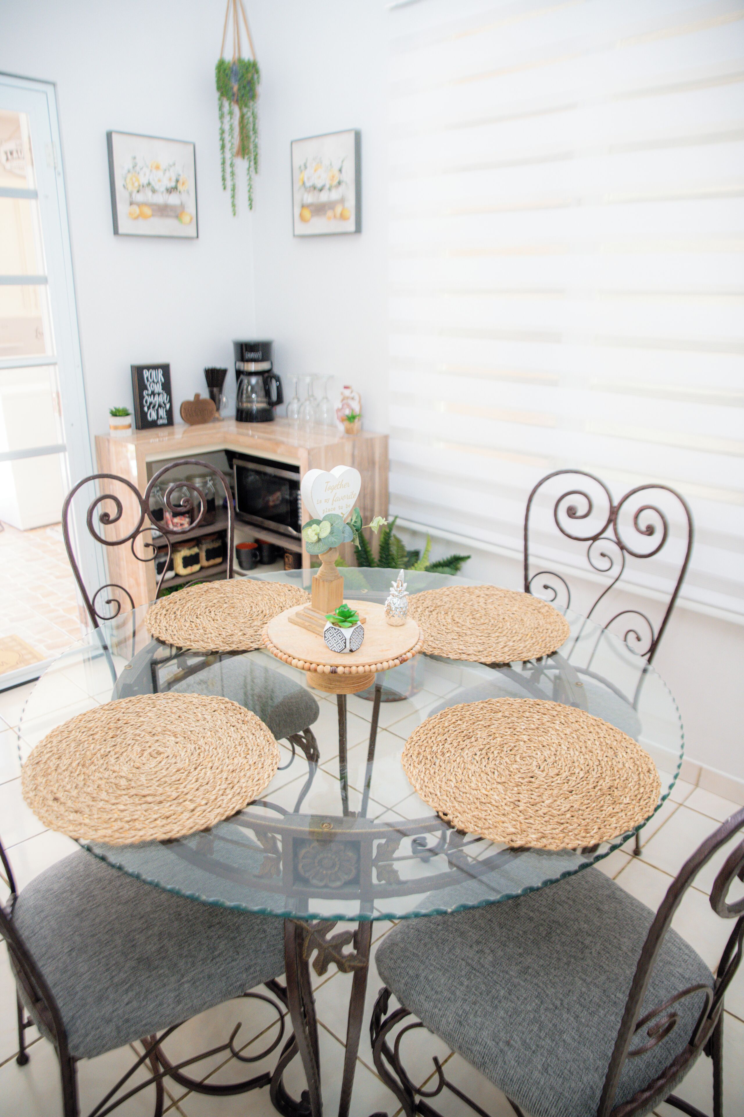 Une table ronde en verre, surmontée de sets de table en fibres tressées, entourée de chaises en métal dotées d’assises rembourrées.