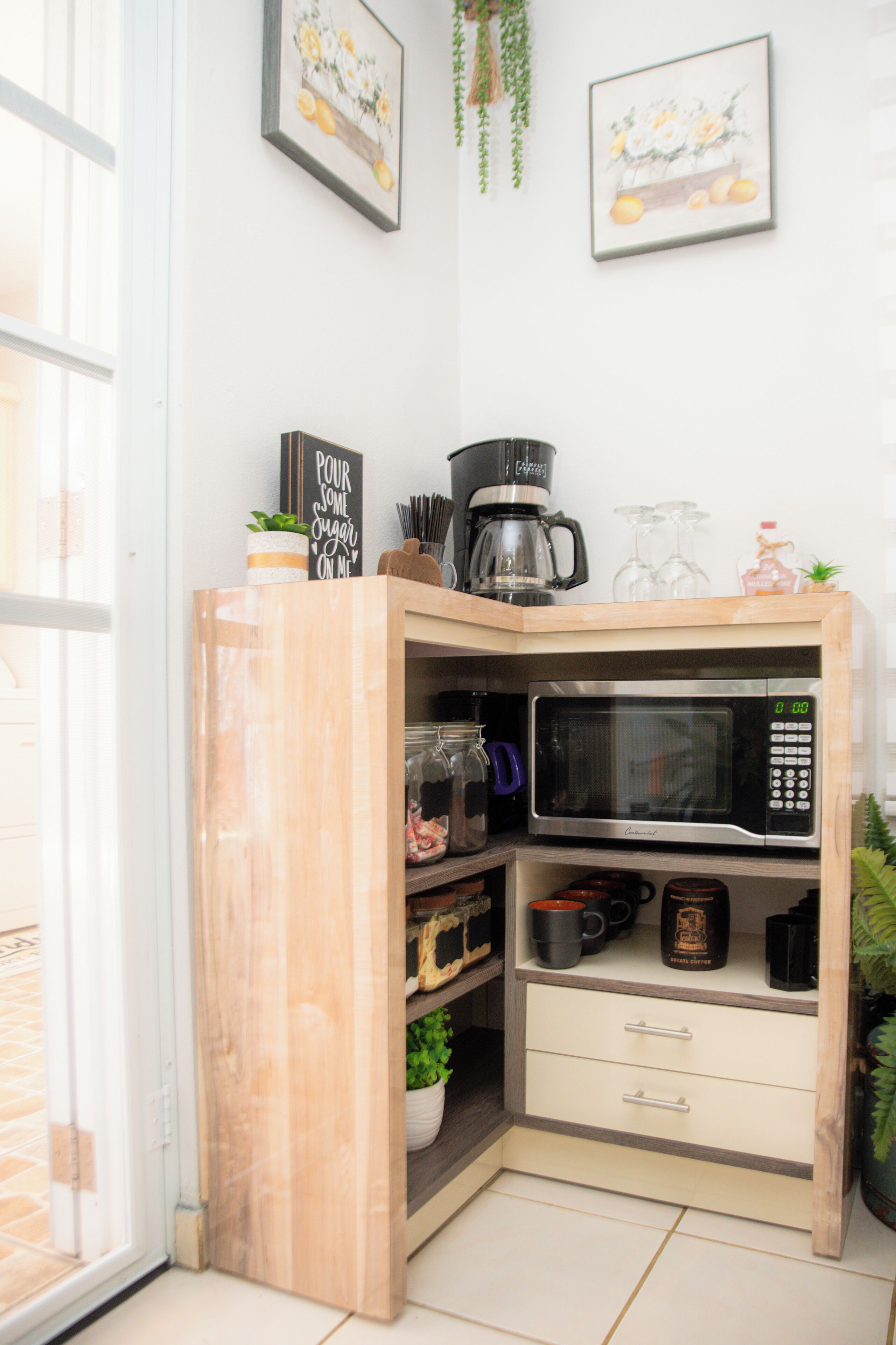 A corner kitchen with a microwave, coffee maker, and storage shelves.