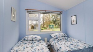 Une chambre avec deux lits simples, une fenêtre donnant sur l’extérieur et une petite table placée entre les lits.