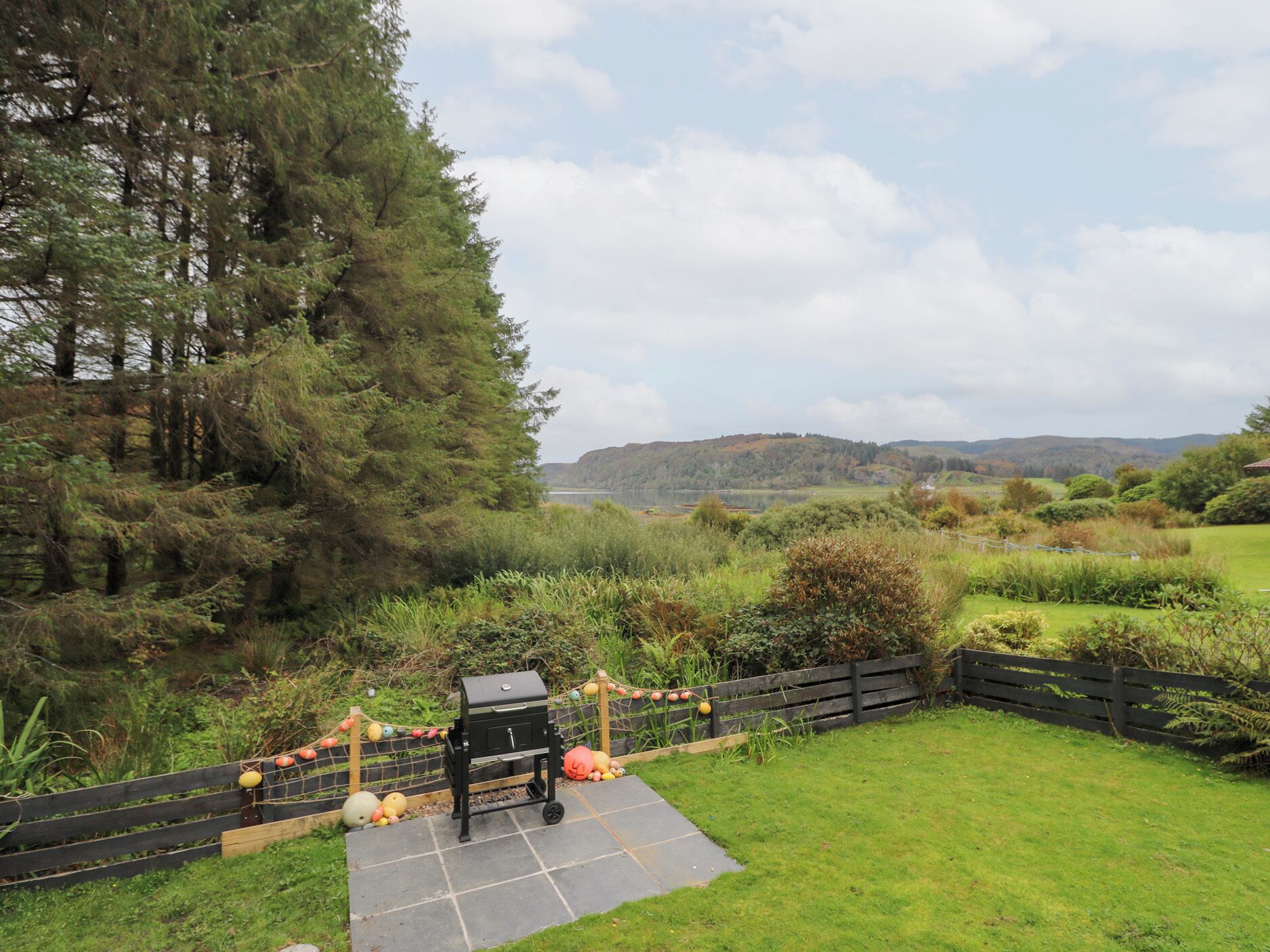 A backyard with a barbecue grill, a wooden fence, and a view of hills in the distance.