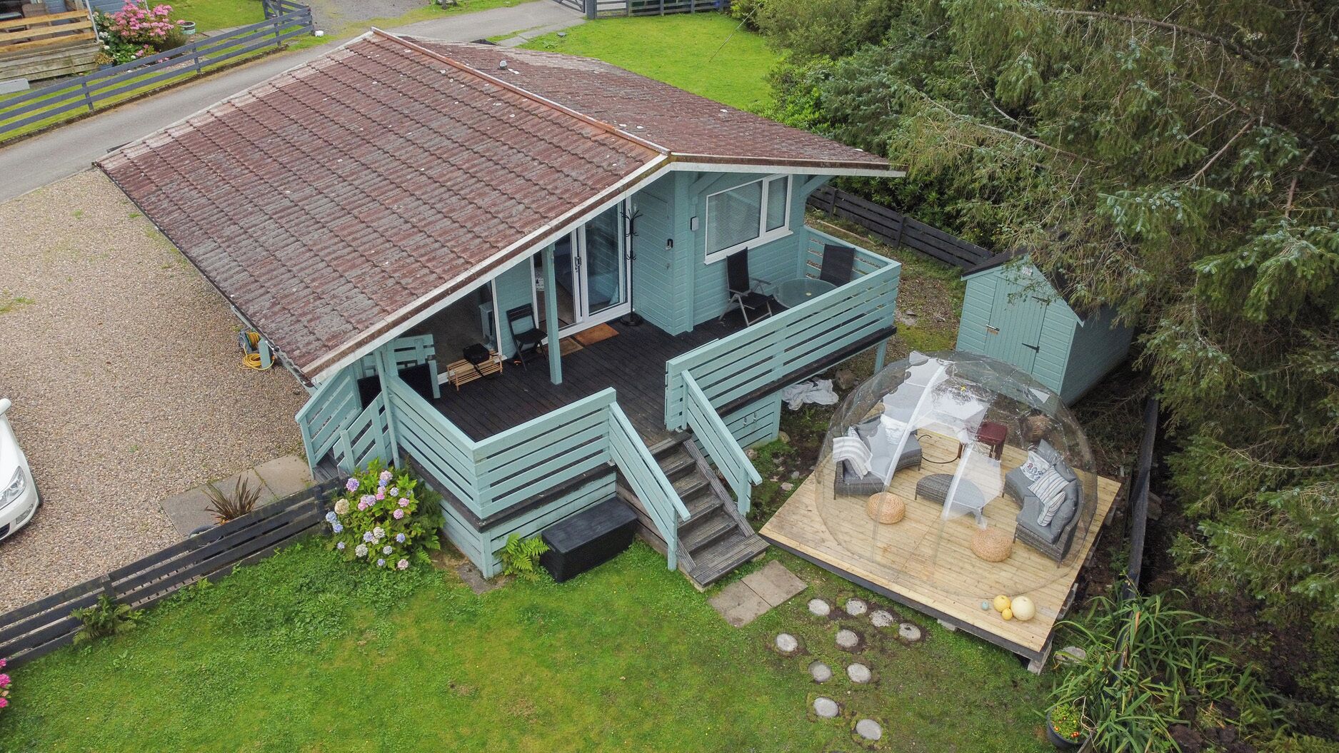 Uma casa azul clara com varanda, área de estar coberta ao ar livre e um pequeno jardim com flores.