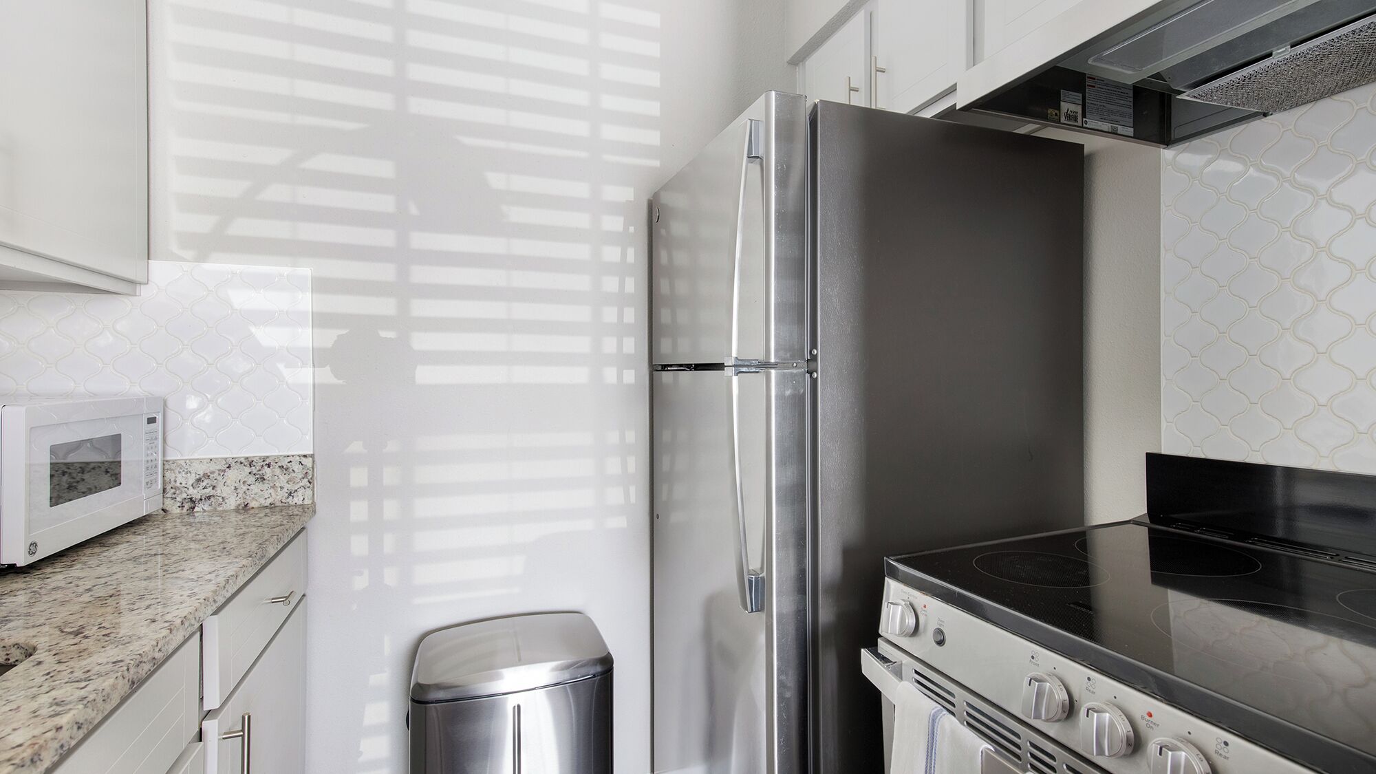 A modern kitchen with white cabinetry, a stainless steel refrigerator, a microwave, a gas stove, and a trash can.