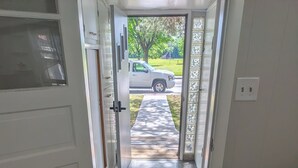 Une porte donnant sur une allée où est garé un véhicule, un tapis devant l’entrée et un bureau avec des papiers.