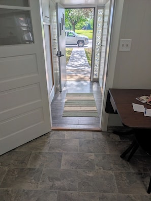 A doorway leading to a driveway with a parked vehicle, a rug on the entrance, and a desk with papers.