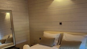 Een slaapkamer met houten lambrisering, een bed met veel kussens, een nachtkastje met spiegel, en een wandlamp.