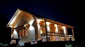 Een houten vakantiehuis met een overdekte veranda en meerdere ramen, verlicht in de nacht.
