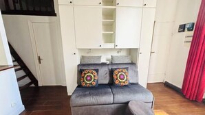 Un sofá gris con dos cojines decorativos, un mueble de almacenaje blanco y una cortina roja.