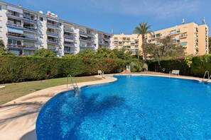 Une piscine à bord incurvé, entourée d’une pelouse bien entretenue et de haies.