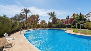 A swimming pool with a curved edge, surrounded by well-maintained hedges and palm trees. - 'Marbella City Center Apartment' with Sea View, Shared Pool and Wi-Fi (Marbella)