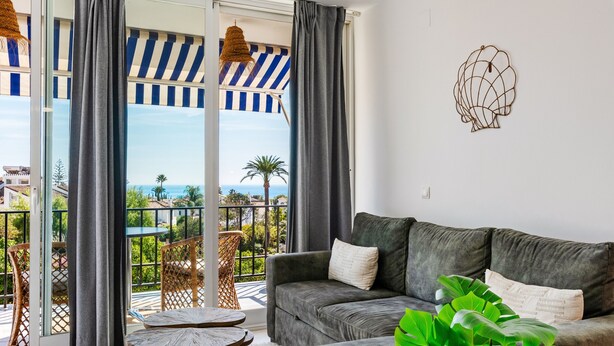 A living room with a grey sofa, a small table, and a balcony with a striped awning. - 'Marbella City Center Apartment' with Sea View, Shared Pool and Wi-Fi (Marbella)