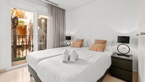 Habitación de hotel con una cama grande, dos mesitas de noche, una ventana con vista a un balcón y una puerta.