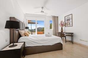 Une chambre d’hôtel équipée d’un lit, d’un bureau, d’une chaise, d’un ventilateur de plafond et d’une fenêtre donnant sur un paysage agréable.