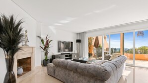 Una sala de estar moderna con sofá, televisión, chimenea y ventanas amplias.