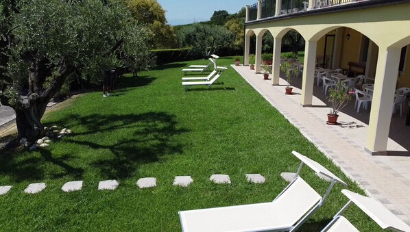 A courtyard with a lawn, outdoor seating, and a building with arches. - AGRITURISMO MONTEMAGGIO (Lapedona)